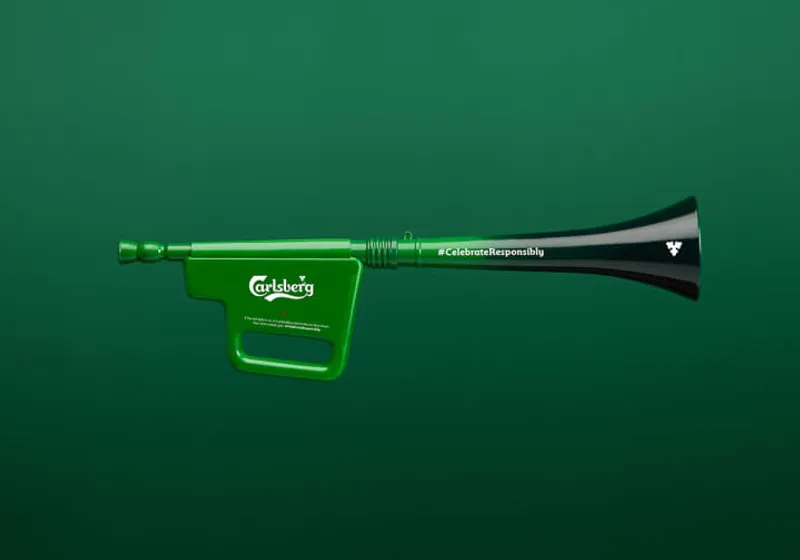 A green vuvuzela with the Carlsberg logo on the handle, set against a matching green background. The instrument features the hashtag '#CelebrateResponsibly' on the horn, promoting responsible celebration.